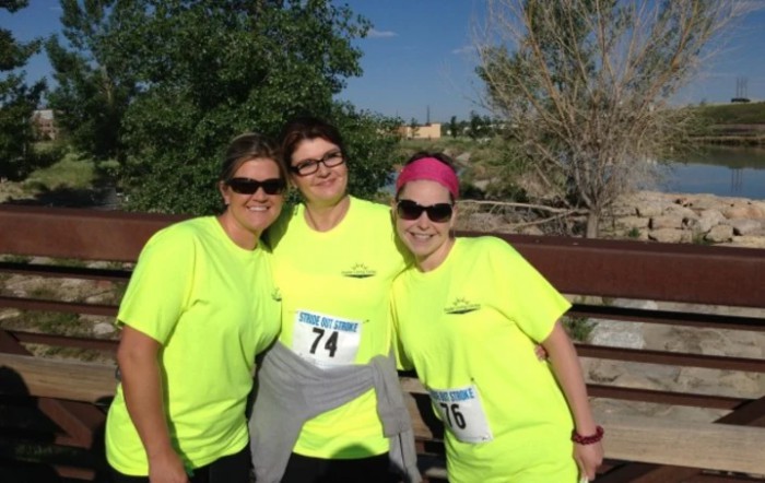 Three friends posing together outdoors in bright running attire during a race event.