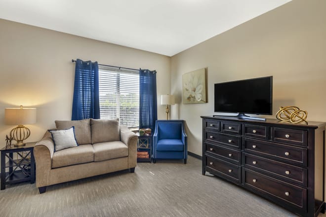 A cozy living room featuring a sofa, armchair, TV, and a large dresser with a window view.