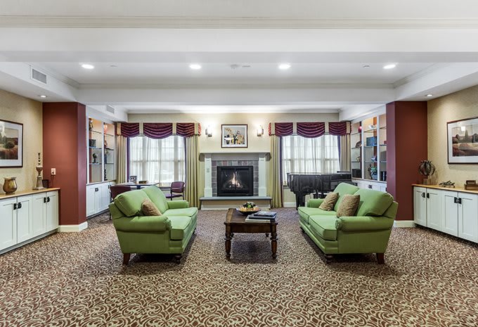 A spacious living room with twin green sofas facing a central fireplace, decorated with patterned carpet and elegant curtains.