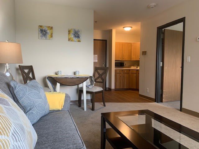 A cozy living room featuring a sofa, coffee table, and a small dining area leading to the kitchen.