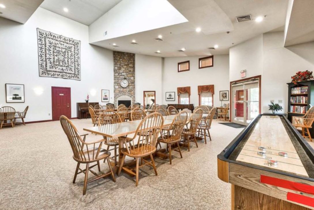 A spacious lounge area with wooden furniture, featuring a large dining table and chairs, a stone fireplace, and recreational amenities.
