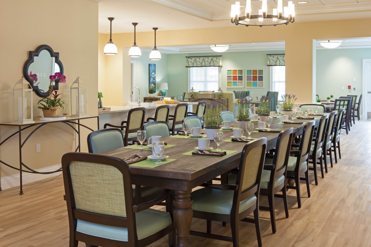 A well-decorated dining room with a long table and multiple chairs, set for a meal, featuring elegant lighting and decor.