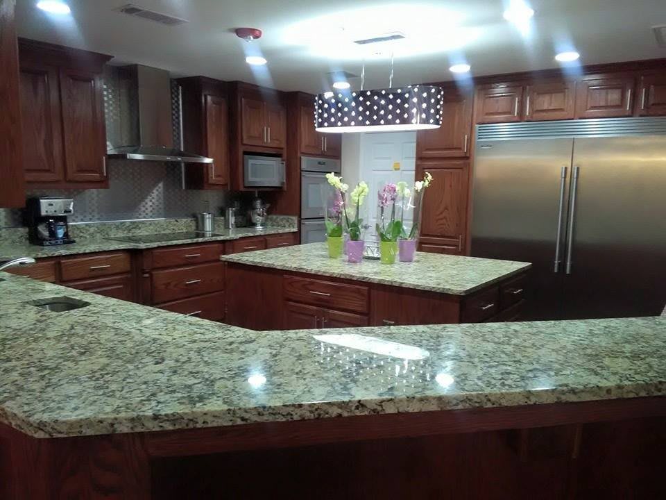A modern kitchen with granite countertops and wood cabinets, featuring stainless steel appliances and pendant lighting.