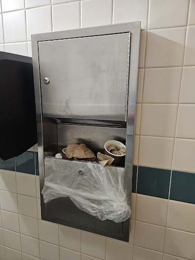 A metal trash receptacle overflowing with waste in a restroom.