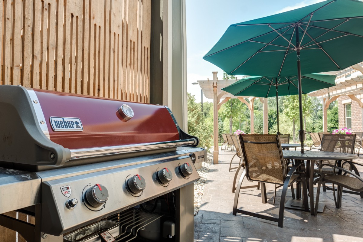 An outdoor patio setup with a barbecue grill and dining furniture under an umbrella.