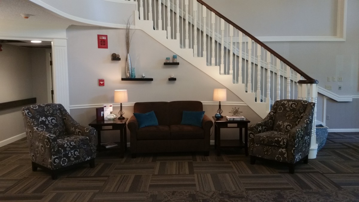 A cozy living room area with a sofa, chairs, and lamps under a staircase.