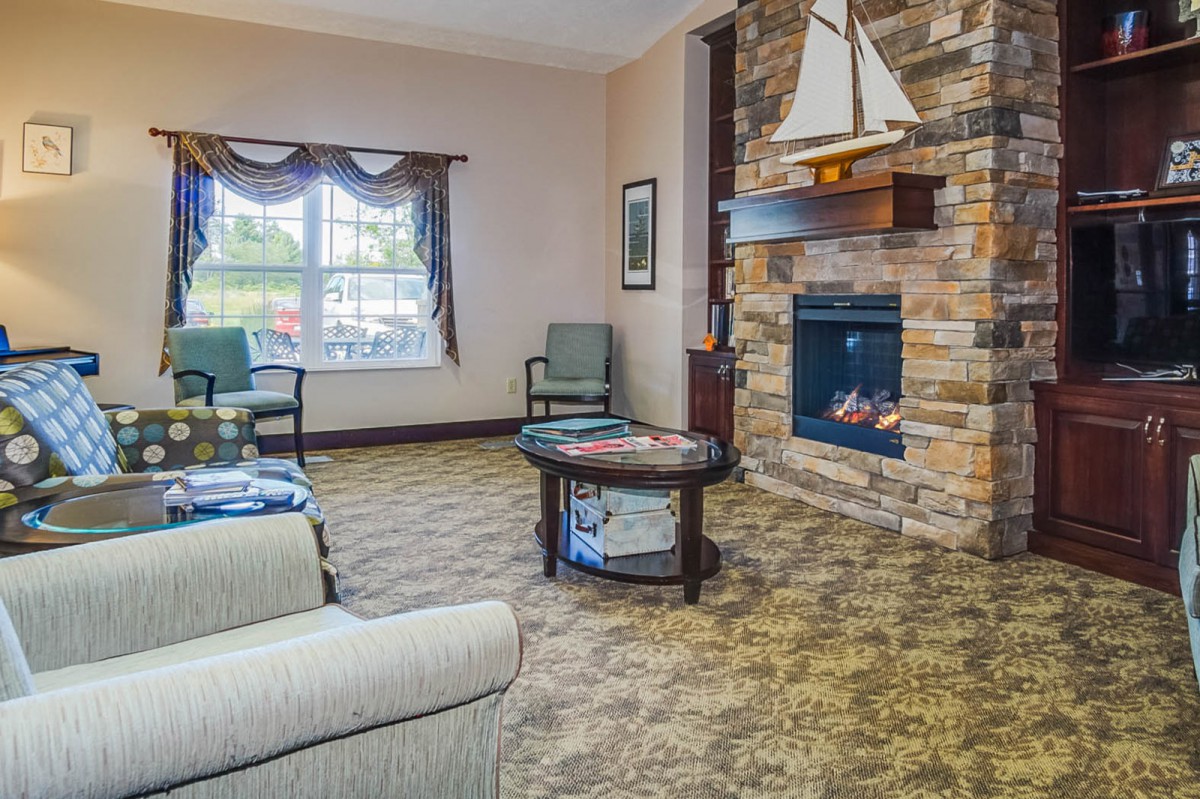 A cozy living room with a stone fireplace, comfortable seating, and natural light streaming in through the window.