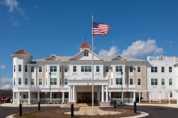 A large building with classical architecture and an American flag flying in front under a blue sky.