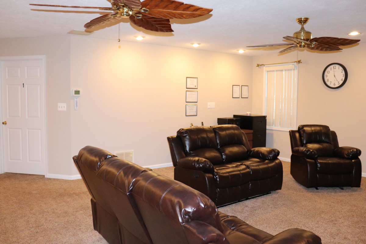 A cozy living room with leather sofas, ceiling fans, and carpet flooring.