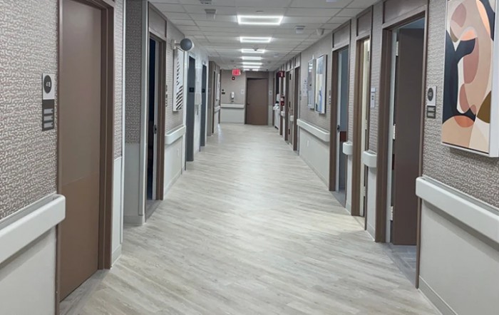 A long hospital corridor with multiple doors and bright fluorescent lighting.