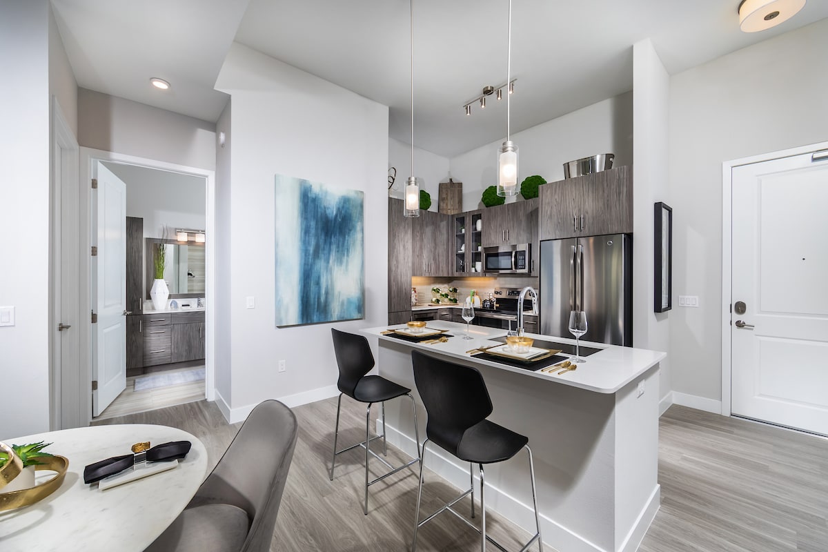 A modern kitchen with a sleek design featuring a dining area, pendant lights, and contemporary artwork.