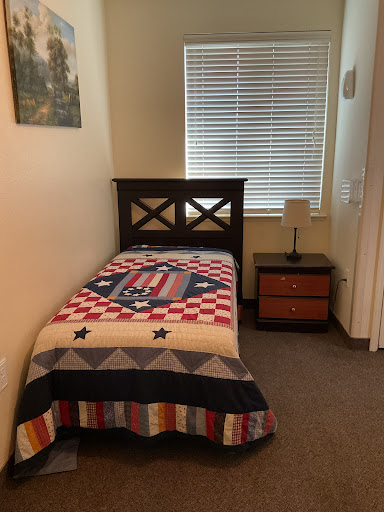 A cozy single bedroom featuring a patterned quilt and a bedside lamp.