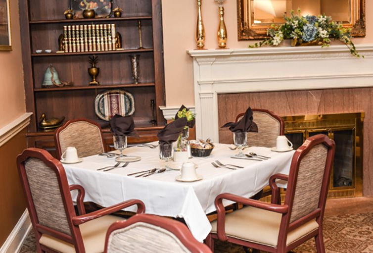 An elegantly set dining table in a formal dining room with a fireplace and bookshelf in the background.