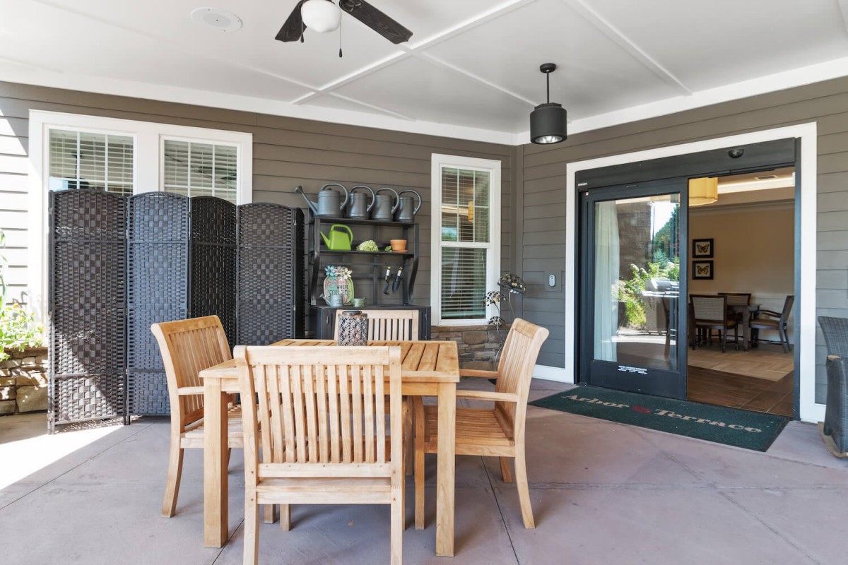 A cozy outdoor patio area featuring a wooden dining set, potted plants, and storage shelves.