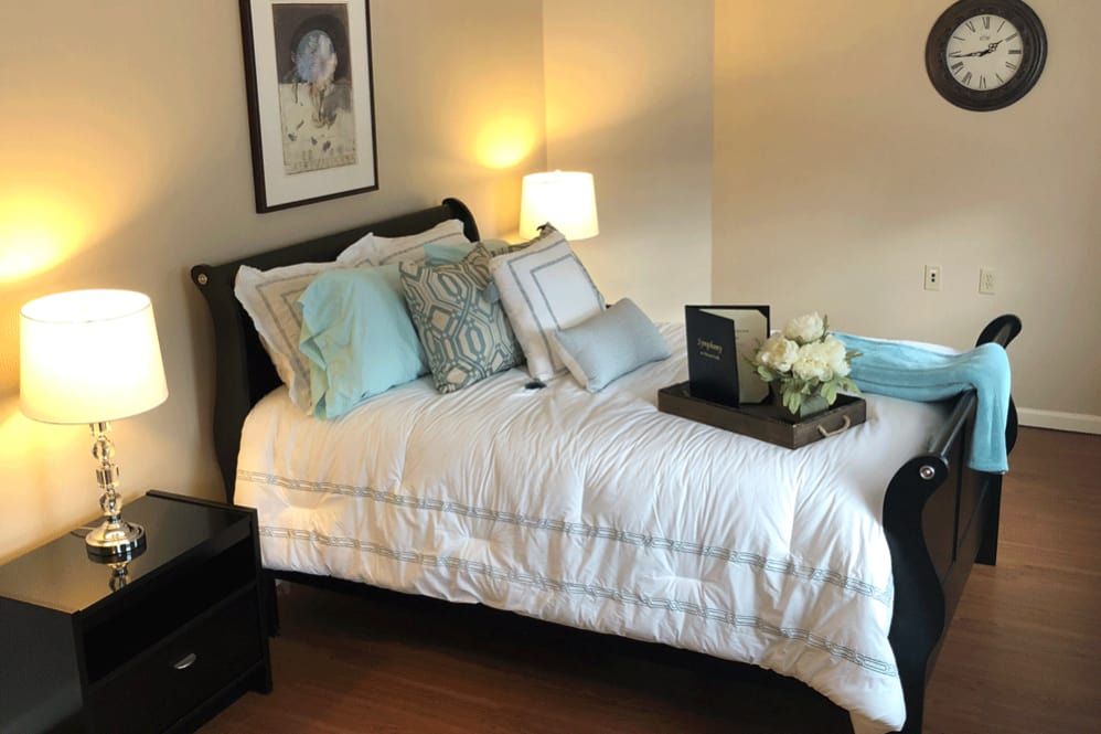 A cozy bedroom scene with a neatly made bed adorned with decorative pillows and a bedside lamp casting warm light.