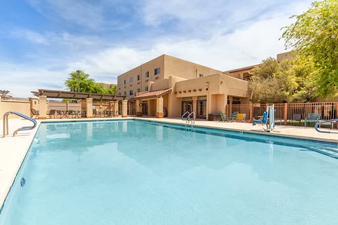 An outdoor swimming pool adjacent to a hotel building under a clear blue sky.