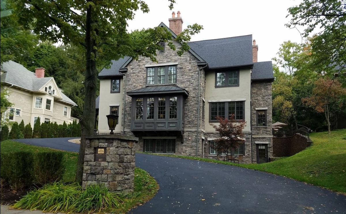 A large stone house with a curved driveway and surrounding trees.