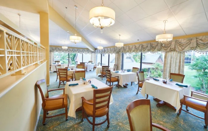 A bright and elegant dining area with neatly arranged tables and chairs, surrounded by large windows.