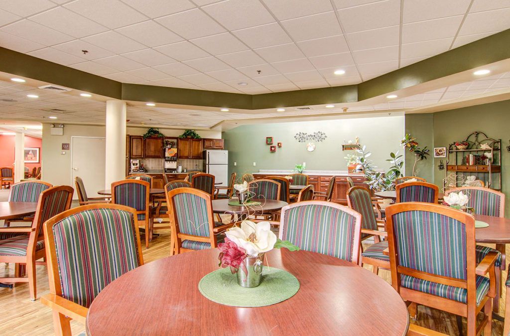 A communal dining area with multiple tables and chairs, featuring a small kitchen section in the background.