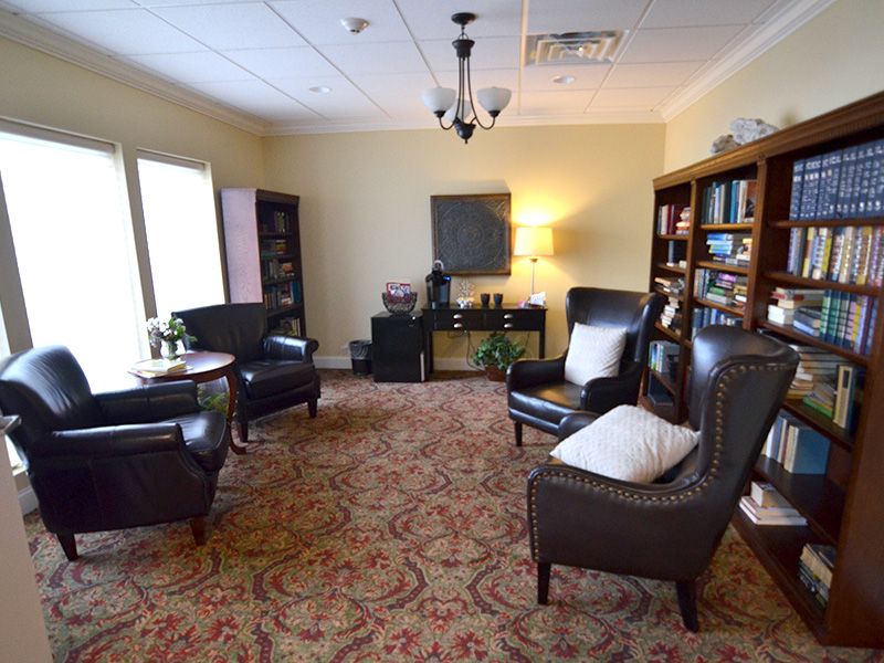 A cozy waiting room with leather chairs, bookshelves, and a patterned carpet.