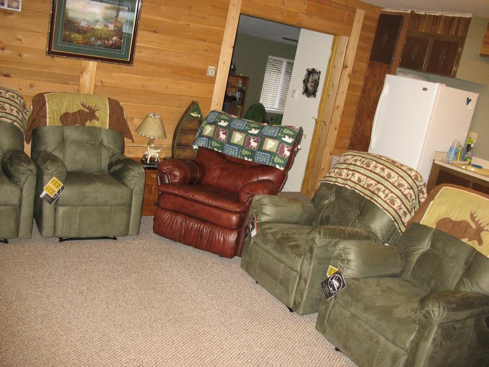 A cozy living room with comfortable chairs and wood paneling, styled in a cabin-like design.