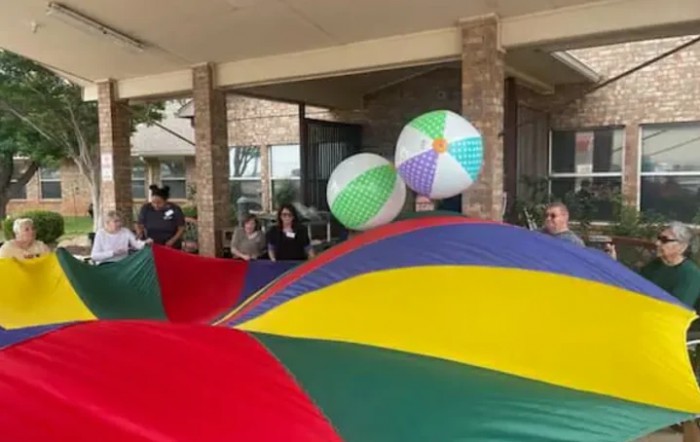 A group of people engaged in a fun outdoor activity with a colorful parachute and beach balls.