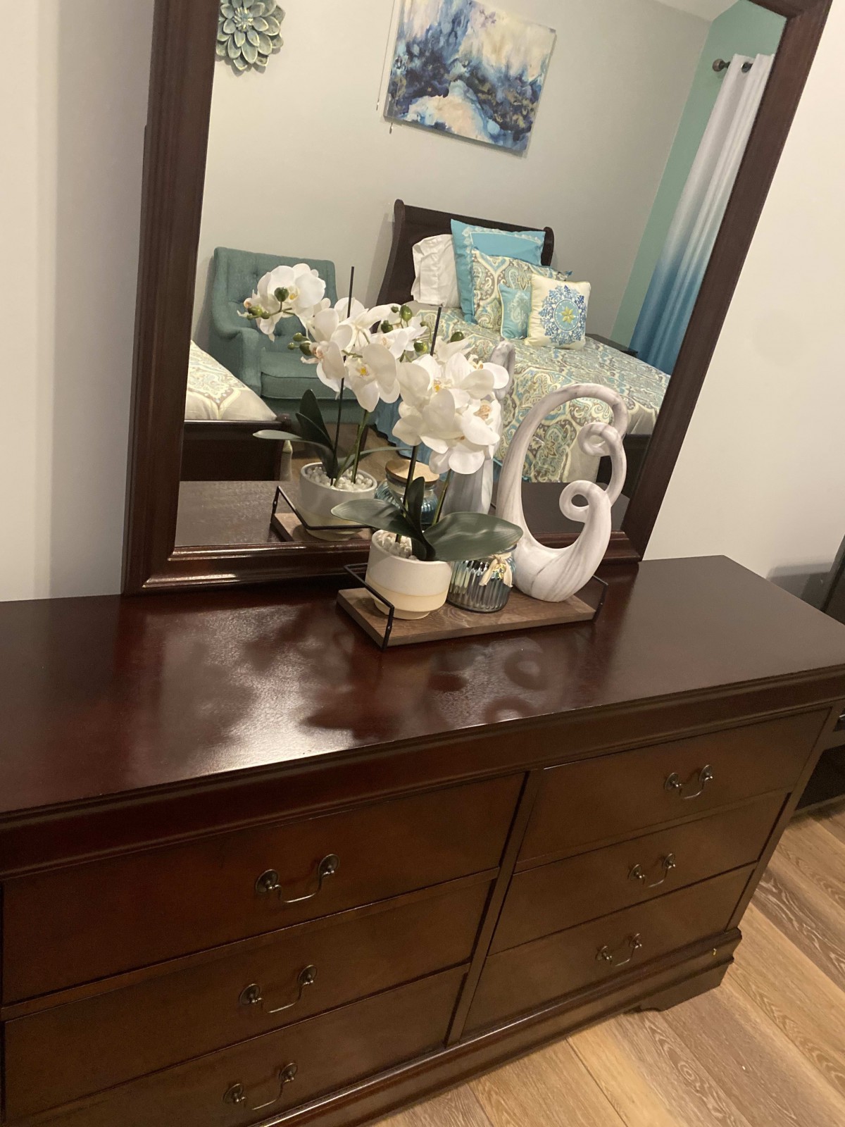 A wooden dresser with decorative flowers and ornaments in front of a mirror.