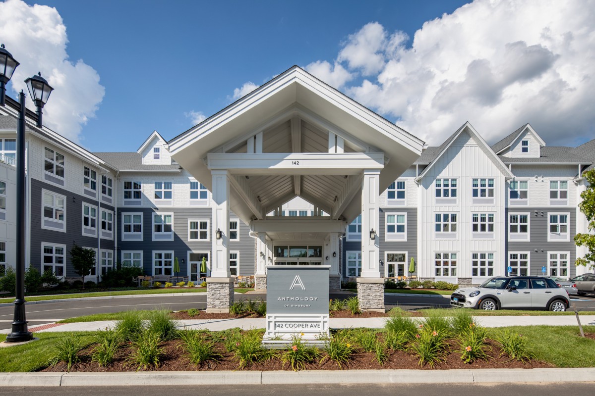 A modern residential building with a covered entrance and well-maintained landscaping under a bright blue sky.