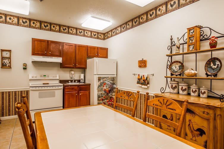 A cozy kitchen and dining area with wooden cabinets, a white stove and refrigerator, and country-themed decor.