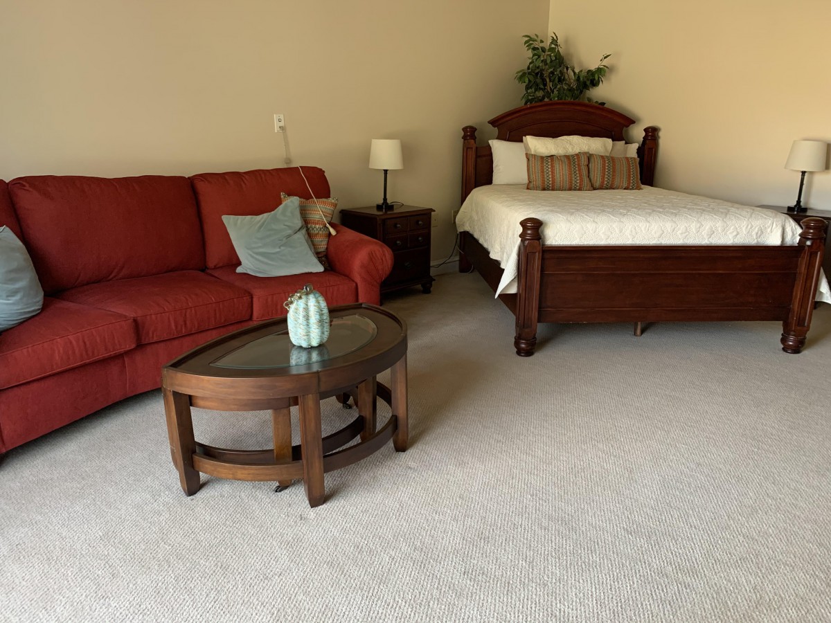 A cozy room featuring a red sofa, wooden bed, and small coffee table.