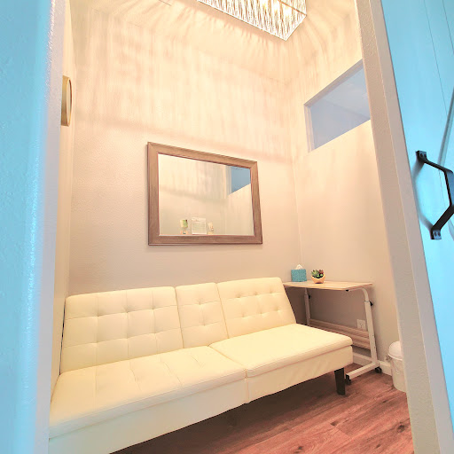 A cozy waiting area featuring a modern white sofa, a large mirror, and elegant lighting.
