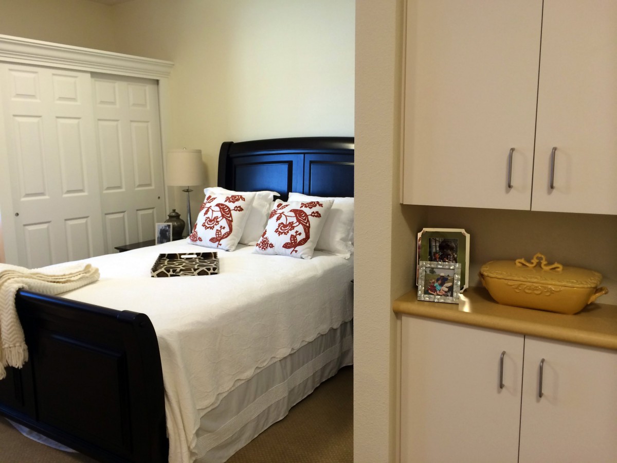 A cozy bedroom with a neatly made bed, decorative pillows, and a nightstand featuring a lamp and photo frame.