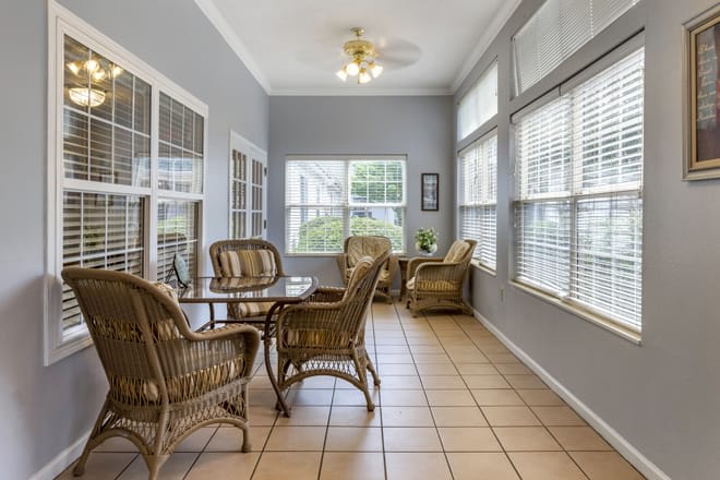 A bright sunroom featuring wicker furniture and large windows, allowing ample natural light.