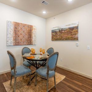 A cozy dining area with a round table and four upholstered chairs, complemented by two pieces of artwork on the walls.