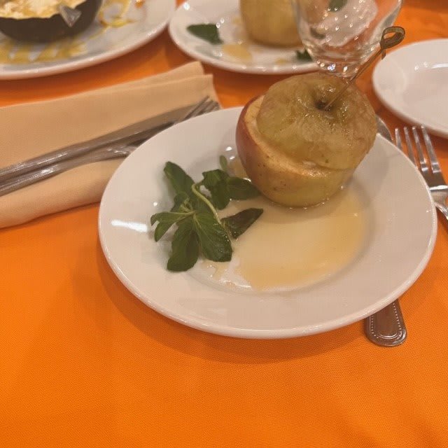 A plated dessert featuring a baked apple with sauce and mint garnish on a table.