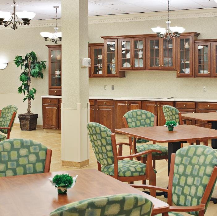 A well-organized dining area with wooden tables, patterned chairs, potted plants, and glass-front cabinets.