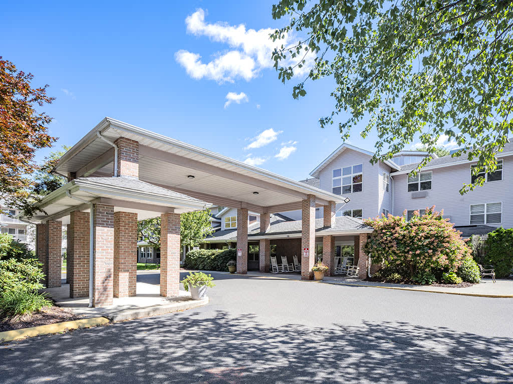 A residential building with a covered entrance and driveway, surrounded by trees under a clear sky.