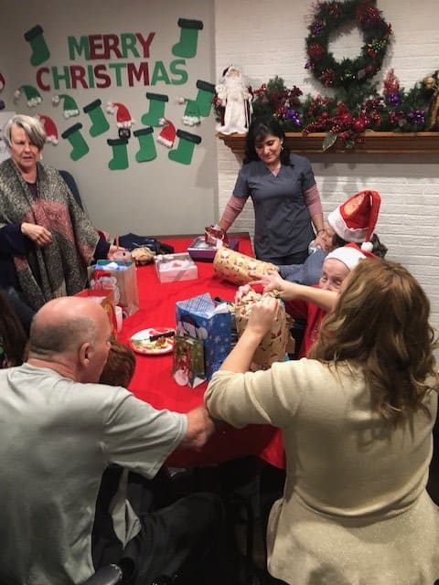 A family gathers around a festive table exchanging gifts during a Christmas celebration.