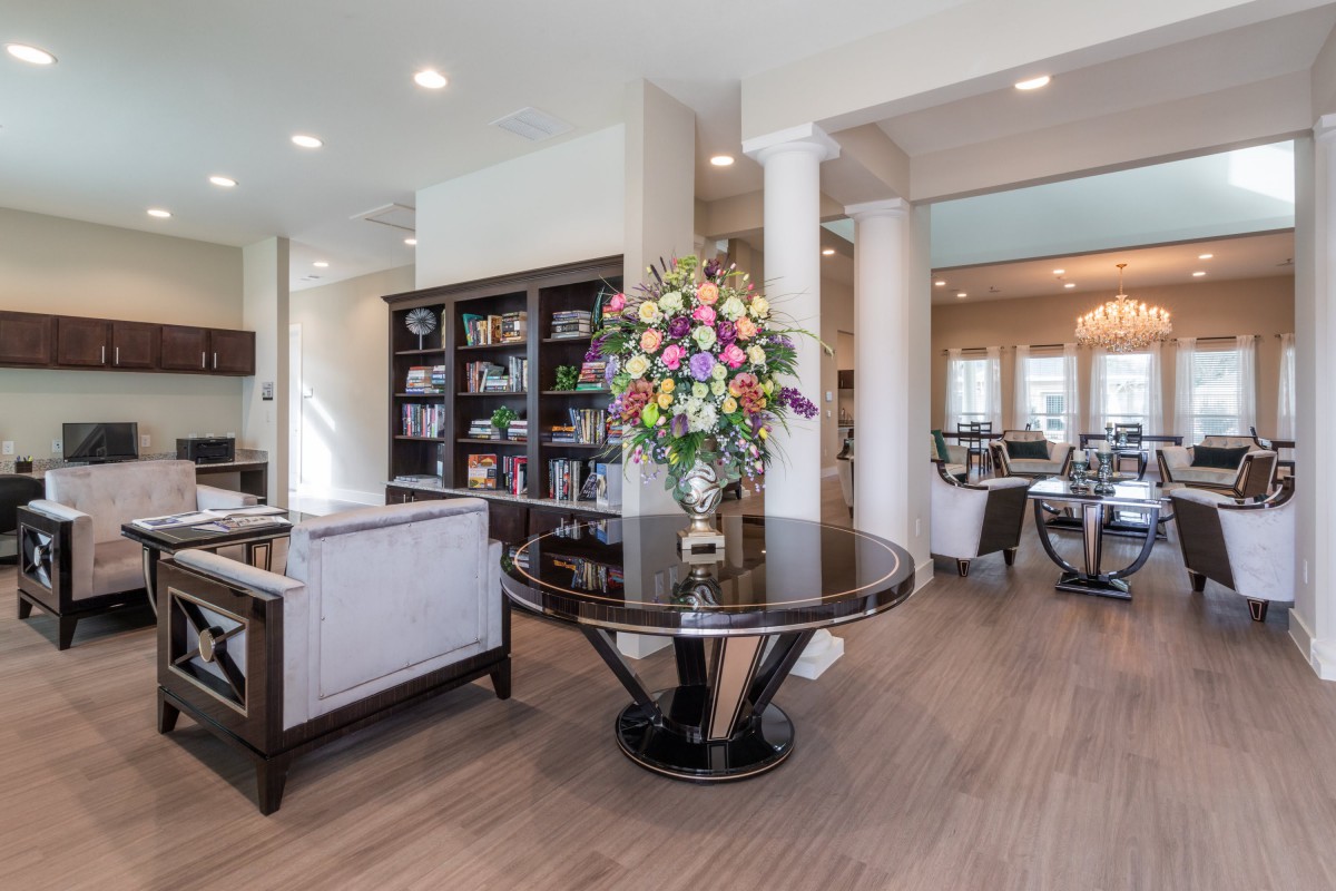 A modern living room with elegant decor, featuring a central table with a floral arrangement and a bookshelf in the background.