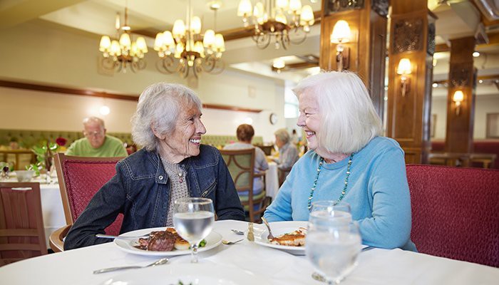 Two elderly women enjoy a meal and conversation in a restaurant.