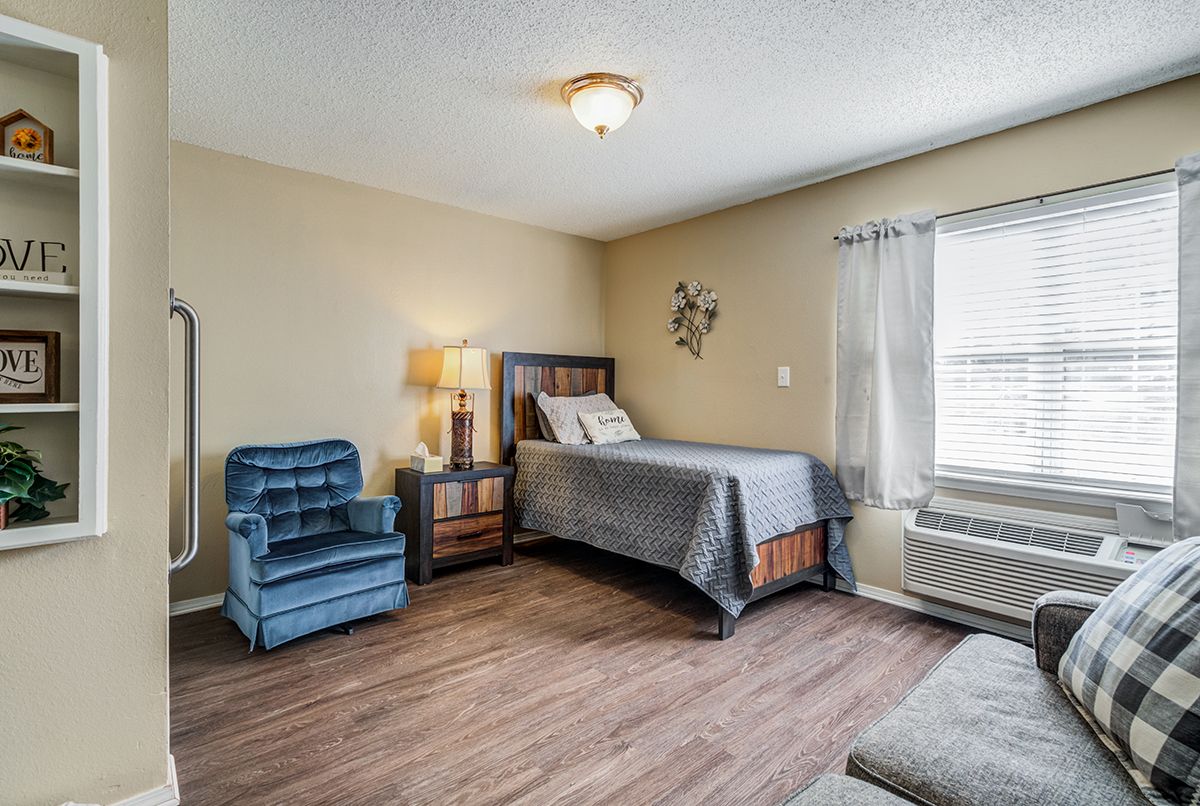 A cozy bedroom with a bed, armchair, and wooden flooring.