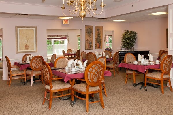 A cozy dining room setup with elegantly decorated tables and wooden chairs, featuring a chandelier hanging from the ceiling.