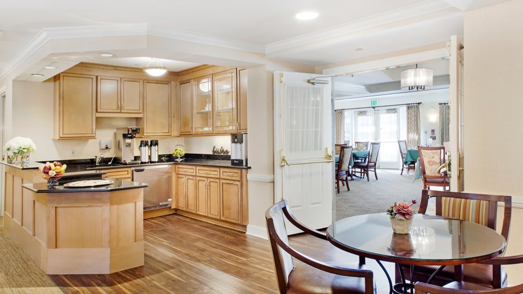 A modern kitchen with wooden cabinets opens into a spacious dining area, featuring hardwood floors and abundant natural light.