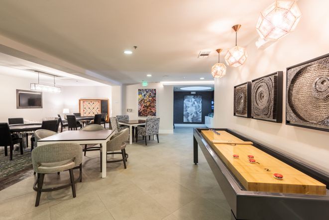 A modern game room featuring a shuffleboard table, contemporary artwork, and comfortable seating.