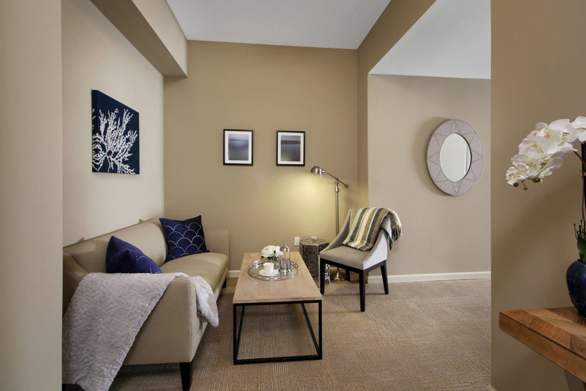A cozy living room with modern decor, featuring a sofa, armchair, coffee table, and artwork on the walls.
