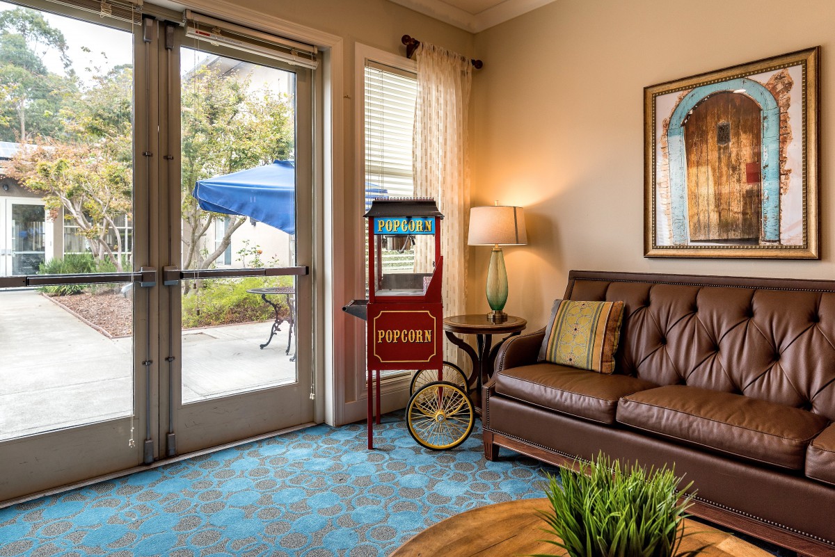 A cozy living room featuring a vintage popcorn machine, leather sofa, and soft lighting from a lamp near a window with a view outside.