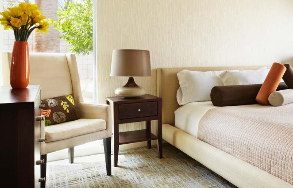 A cozy bedroom with a neutral color palette, featuring a comfortable chair, a nightstand with a lamp, and a neatly made bed.