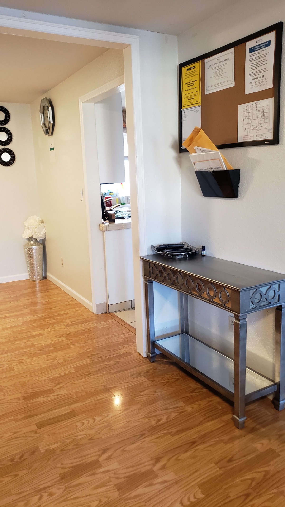 A home hallway with a wooden floor, featuring a decorative table and wall-mounted mail holder.