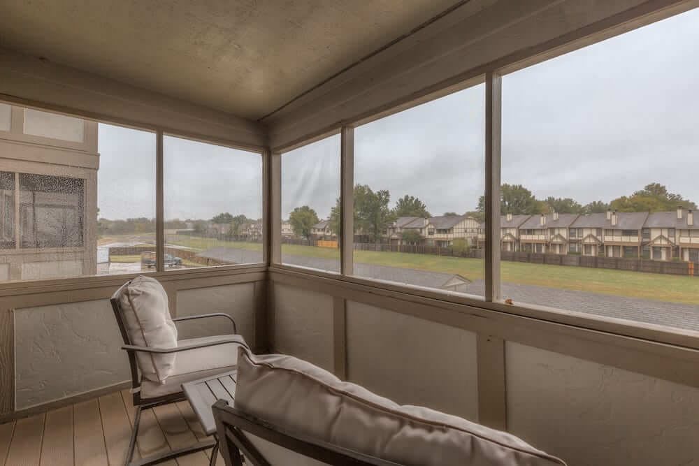 A cozy screened porch with comfortable seating and a view of suburban houses.