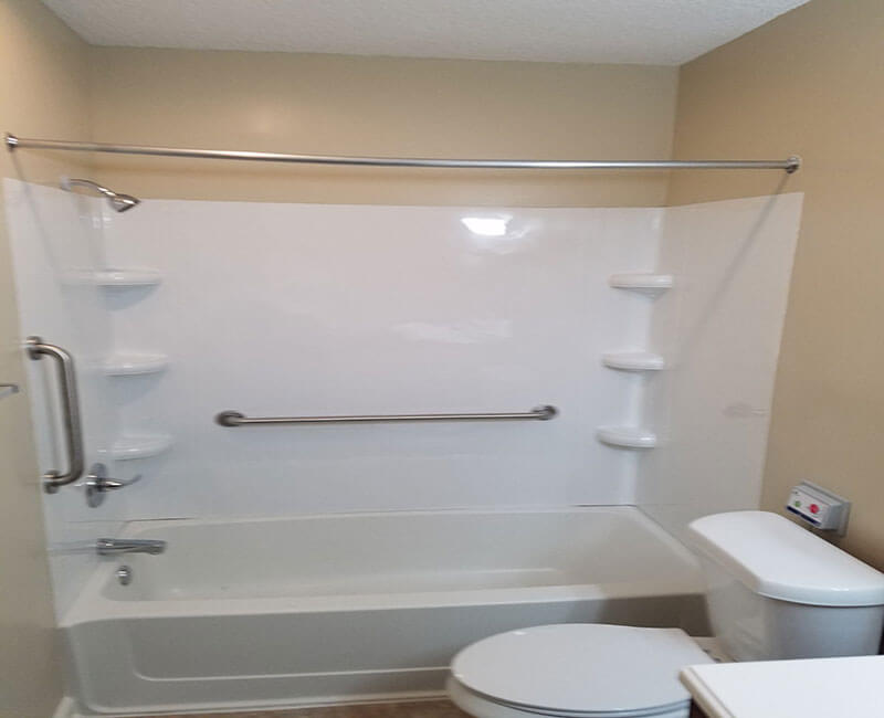 A modern bathroom featuring a combined bathtub and shower with shelving, along with a toilet.